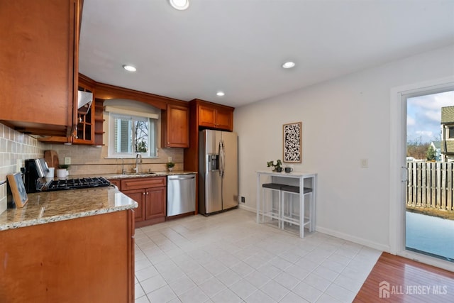 kitchen with sink, light tile patterned floors, appliances with stainless steel finishes, backsplash, and light stone counters