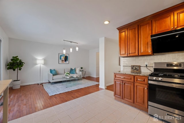 kitchen with backsplash, hanging light fixtures, light hardwood / wood-style floors, stainless steel gas range oven, and light stone countertops