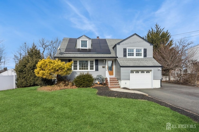 view of front of house with an attached garage, solar panels, fence, driveway, and a front yard