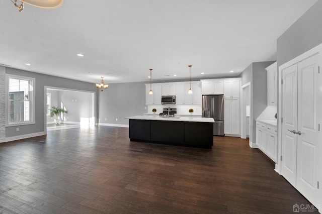 kitchen with stainless steel appliances, dark wood-type flooring, white cabinets, hanging light fixtures, and an island with sink