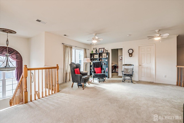 living area with visible vents, an upstairs landing, carpet floors, and ceiling fan