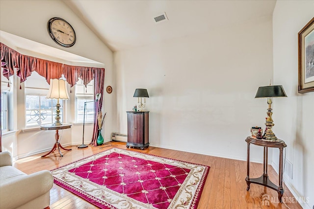 living area with visible vents, a baseboard heating unit, hardwood / wood-style floors, baseboards, and vaulted ceiling