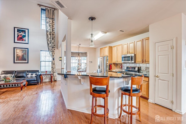 kitchen featuring visible vents, appliances with stainless steel finishes, a kitchen breakfast bar, light wood-type flooring, and backsplash