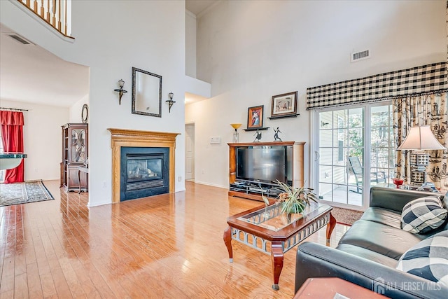 living room with a glass covered fireplace, visible vents, wood finished floors, and a towering ceiling