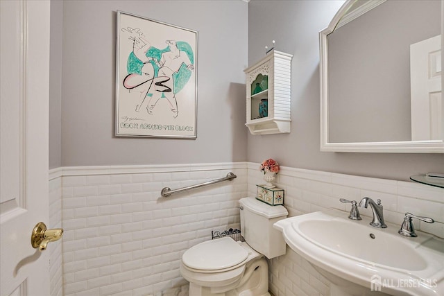 half bath featuring a sink, toilet, tile walls, and wainscoting