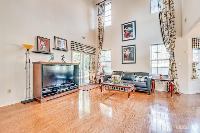 living area with visible vents, baseboards, a towering ceiling, and hardwood / wood-style flooring