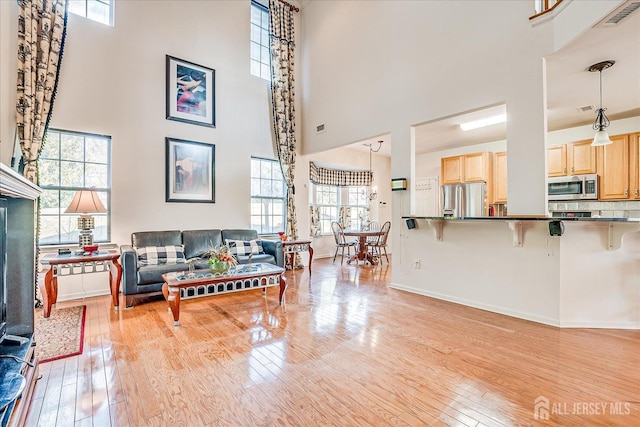 living room featuring visible vents, baseboards, light wood-style flooring, and a towering ceiling