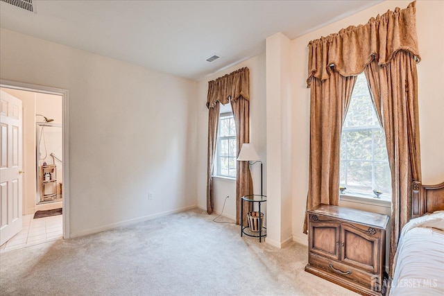 bedroom with visible vents, baseboards, light colored carpet, and connected bathroom