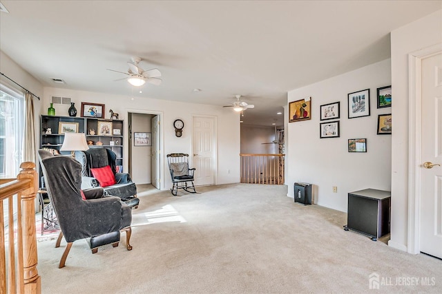 sitting room with an upstairs landing, visible vents, carpet, and a ceiling fan