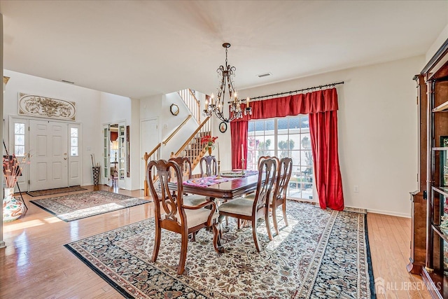 dining space featuring visible vents, stairway, an inviting chandelier, light wood finished floors, and baseboards