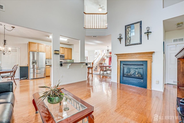 living room with visible vents, light wood-type flooring, an inviting chandelier, and a glass covered fireplace