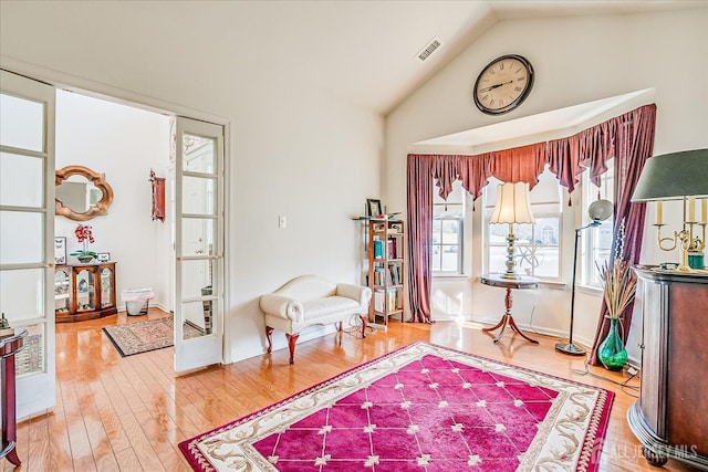 living area featuring visible vents, wood finished floors, baseboards, and vaulted ceiling