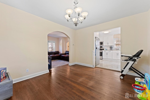 unfurnished dining area with arched walkways, a notable chandelier, wood finished floors, and baseboards