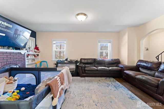 living room featuring arched walkways, wood finished floors, and a brick fireplace