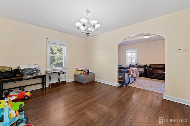game room with arched walkways, radiator heating unit, wood finished floors, and a healthy amount of sunlight