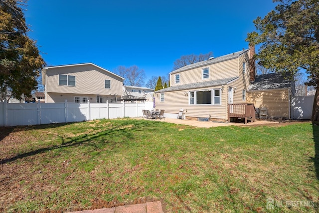 rear view of house with a wooden deck, a lawn, a patio, and fence