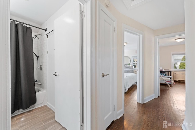 corridor featuring radiator heating unit, baseboards, and wood finished floors