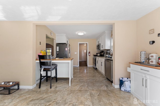 kitchen with stainless steel appliances, baseboards, marble finish floor, and white cabinetry