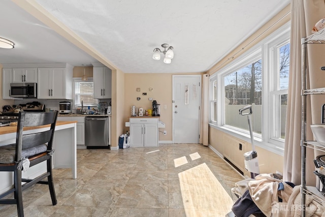 kitchen featuring stainless steel appliances, backsplash, a sink, baseboards, and white cabinetry