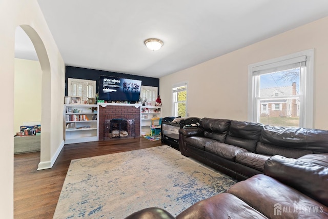 living area with a fireplace, baseboards, arched walkways, and dark wood-type flooring