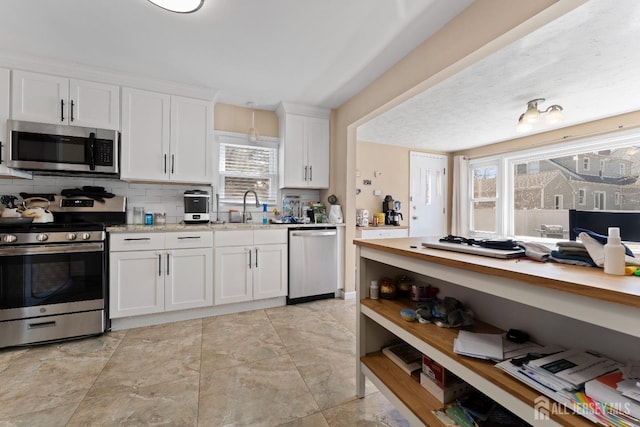 kitchen featuring a sink, decorative backsplash, stainless steel appliances, light countertops, and white cabinets