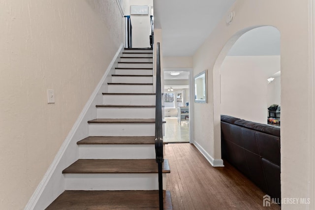 staircase featuring hardwood / wood-style flooring and arched walkways