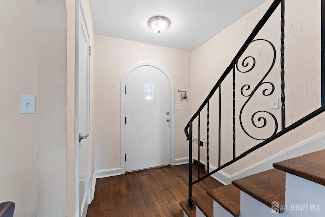 foyer featuring arched walkways, baseboards, wood finished floors, and stairs