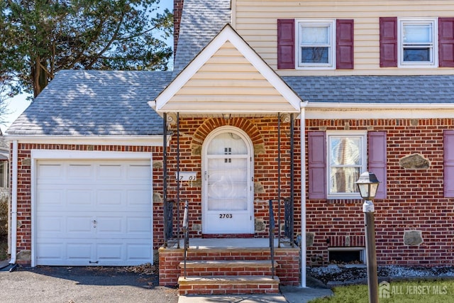 view of front of home with an attached garage, a shingled roof, and brick siding
