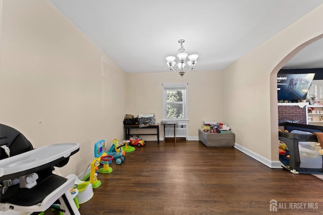 recreation room with arched walkways, radiator, a chandelier, wood finished floors, and a fireplace
