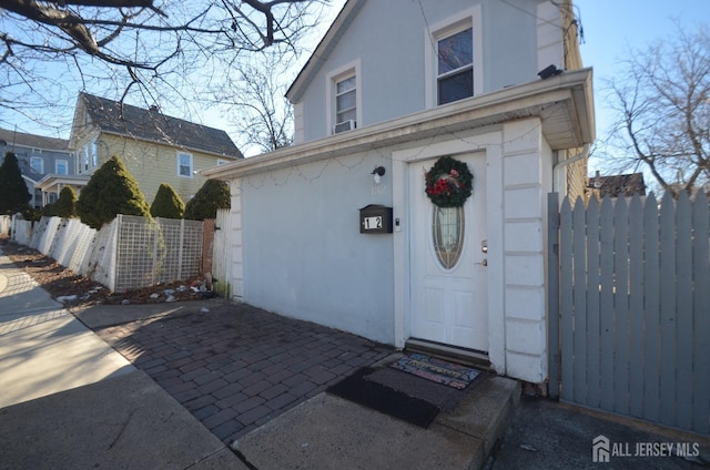 entrance to property featuring fence and stucco siding