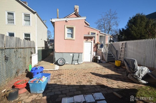rear view of property featuring a fenced backyard, stucco siding, a chimney, and a patio area