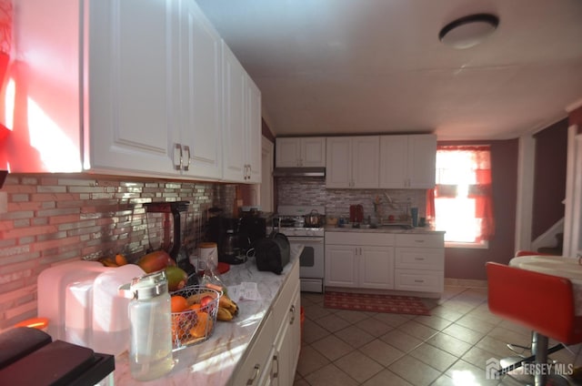 kitchen with tasteful backsplash, light tile patterned flooring, white cabinets, and white stove