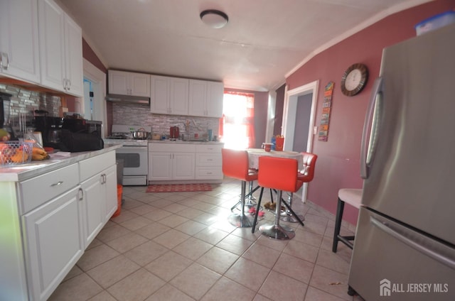 kitchen with under cabinet range hood, white range with gas stovetop, light countertops, freestanding refrigerator, and white cabinets