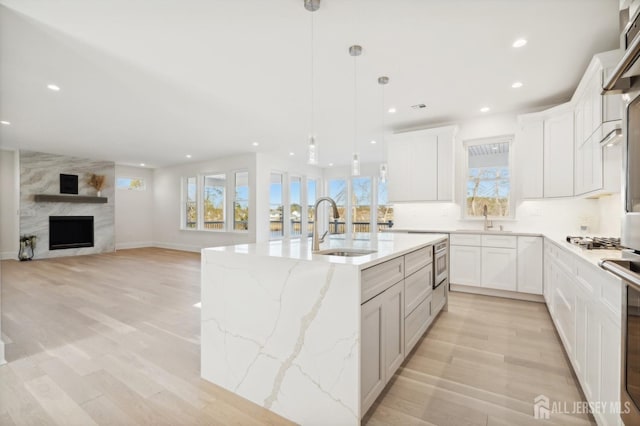 kitchen with hanging light fixtures, open floor plan, white cabinets, a sink, and an island with sink