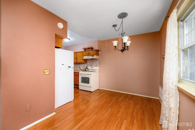 kitchen with white appliances, hanging light fixtures, backsplash, a notable chandelier, and light wood-type flooring