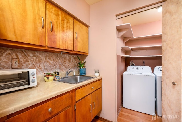 laundry room with washing machine and clothes dryer, light hardwood / wood-style floors, and sink