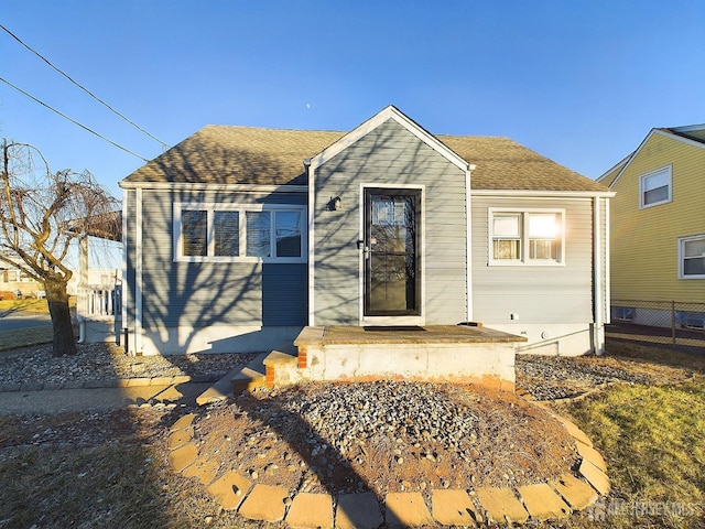 view of front facade with a shingled roof and fence