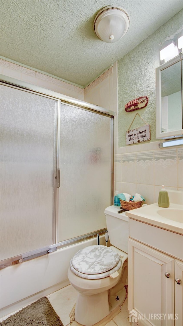 full bathroom featuring vanity, combined bath / shower with glass door, tile patterned flooring, toilet, and tile walls