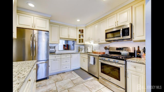 kitchen featuring backsplash, light stone countertops, stainless steel appliances, and a sink