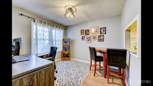 office with light wood-style flooring, a textured ceiling, and baseboards