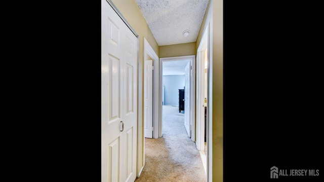 hallway with light colored carpet and a textured ceiling