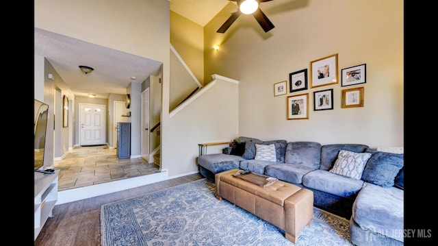 living area featuring baseboards, stairway, a high ceiling, wood finished floors, and a ceiling fan