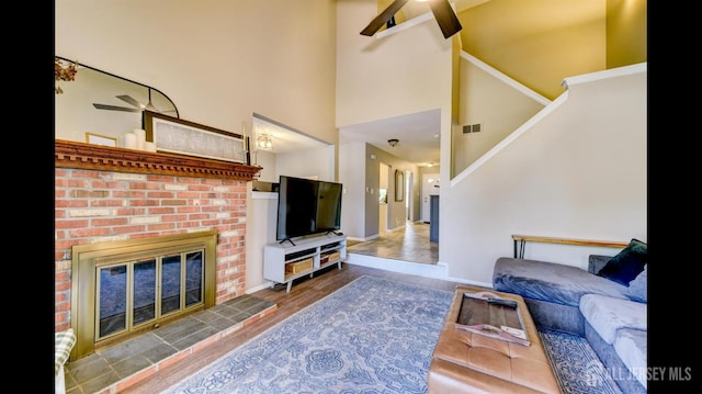 living area with stairway, wood finished floors, visible vents, ceiling fan, and a brick fireplace