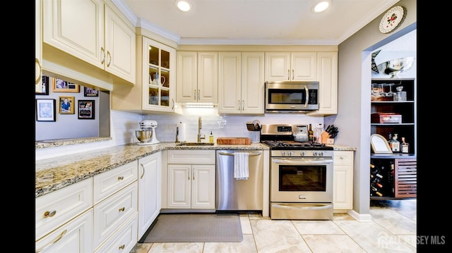 kitchen featuring tasteful backsplash, glass insert cabinets, light stone counters, appliances with stainless steel finishes, and a sink