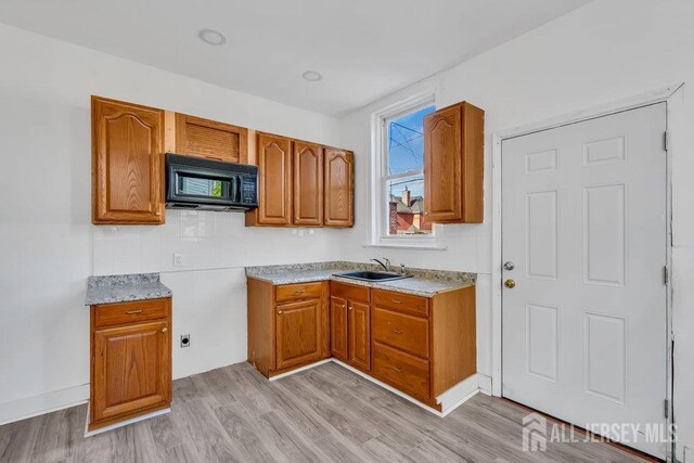 kitchen with sink, light stone counters, and light wood-type flooring