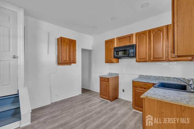 kitchen with brown cabinets, a sink, black microwave, light wood finished floors, and decorative backsplash