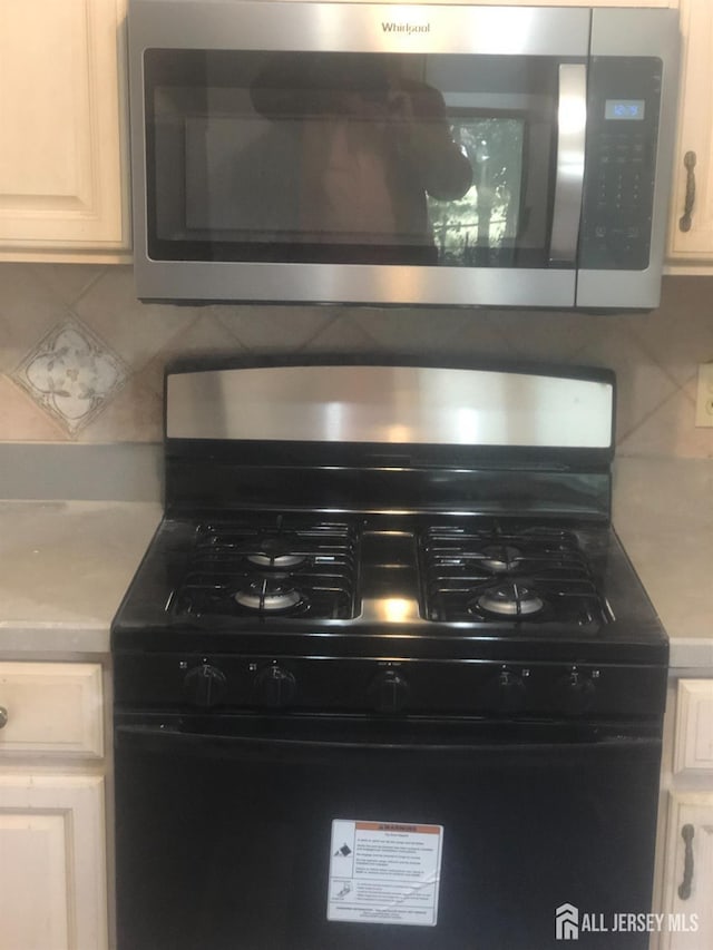 details with black gas range oven, stainless steel microwave, backsplash, light countertops, and white cabinets