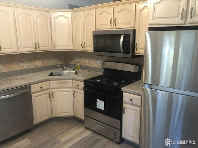 kitchen with appliances with stainless steel finishes, wood finished floors, light countertops, and a sink