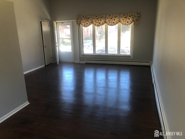 empty room with a baseboard radiator, baseboards, and dark wood finished floors