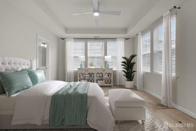 bedroom with a tray ceiling, light colored carpet, and ceiling fan